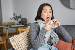 ill woman using spray from sore throat treating her cold flu staying home sick leave sittin