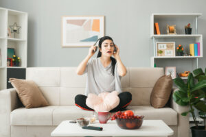 impressed looking side young girl with pillow wearing headphones sitting sofa coffee table living room