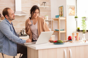 woman looking husband laptop while he is working kitchen girlfriend holding cup coffee happy loving cheerful romantic love couple home using modern wifi wireless internet technology