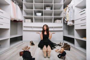 beautiful young woman sitting floor big nice dressing room around shoes doesn t know what wear disappointed tired making choice wearing black dress